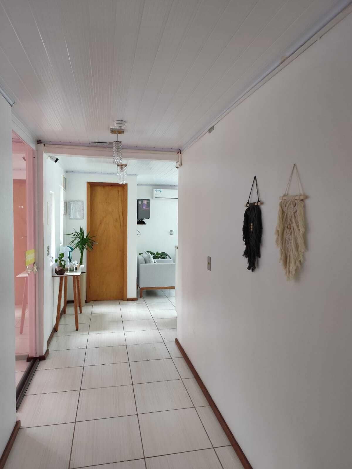 Un pasillo con una puerta de madera, una pequeña mesa con una planta y dos tapices de macramé en la pared.