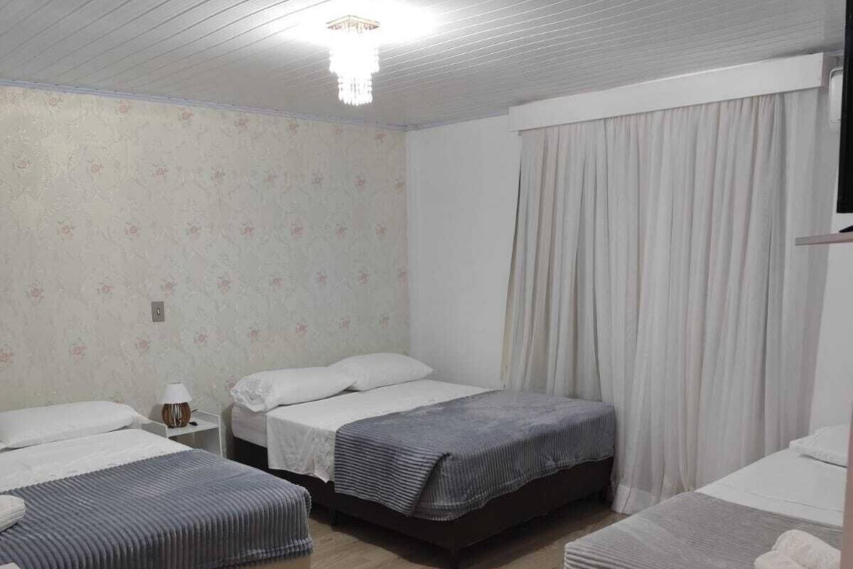 Habitación de hotel con tres camas, piso de madera, televisor de pantalla plana y ventana con cortinas.