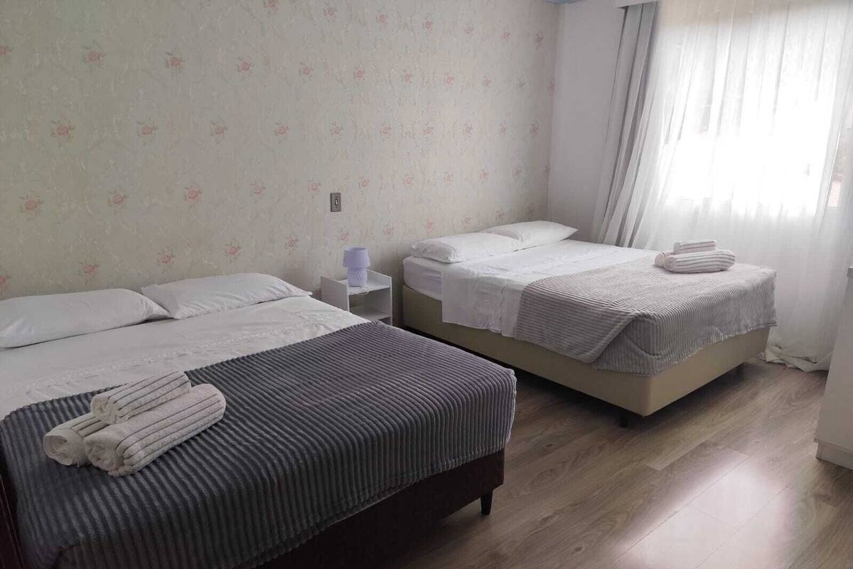 Una habitación de hotel con dos camas, una mesita de noche, una lámpara y un ventanal con cortinas.