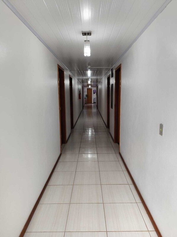 Un pasillo largo y estrecho con paredes blancas y puertas de madera, que conduce a una habitación al final.