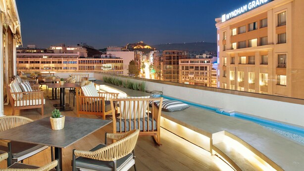 A rooftop terrace with outdoor seating, a pool, and a view of the cityscape at night. - Zeus Essence Wyndham Athens Residence (Athens)