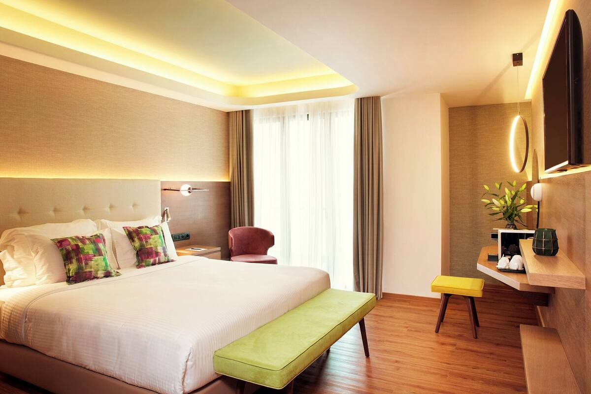 A modern hotel room with a large bed, a bedside table, a desk, and a mirror.