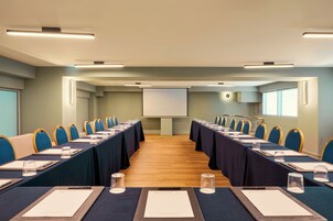 Una sala conferenze con un lungo tavolo, sedie e uno schermo per proiezioni.