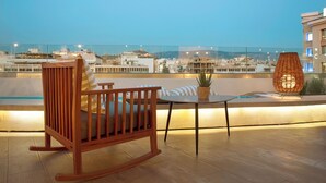 A wooden rocking chair and a small table with a potted plant on a rooftop terrace with a city view. - Zeus Essence Wyndham Athens Residence (Athens)