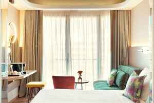 Una camera d'albergo con un letto, una scrivania con una sedia, un tavolino con un vaso e un divano verde con cuscini.