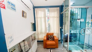A hotel room with a glass door, a white wall with a sign, a patterned rug, and a chair with a cushion. - Hotel Sol de Piura (Piura)