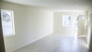 A spacious, empty room with light-colored walls and flooring, large windows, and a door leading to another area. - Los Angeles Extended Stay Hostel (Los Angeles)