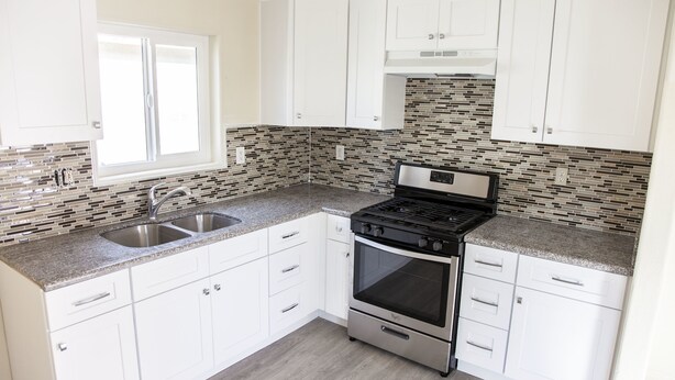A kitchen with white cabinets, a granite countertop, a stainless steel stove, and a tiled backsplash. - Los Angeles Extended Stay Hostel (Los Angeles)