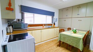 A compact kitchen with a microwave, kettle, and a table set for dining. - Pether Cottage - Talbingo NSW (Talbingo)