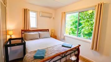 A bedroom with a bed, bedside lamps, a window with curtains, and a view of greenery outside.