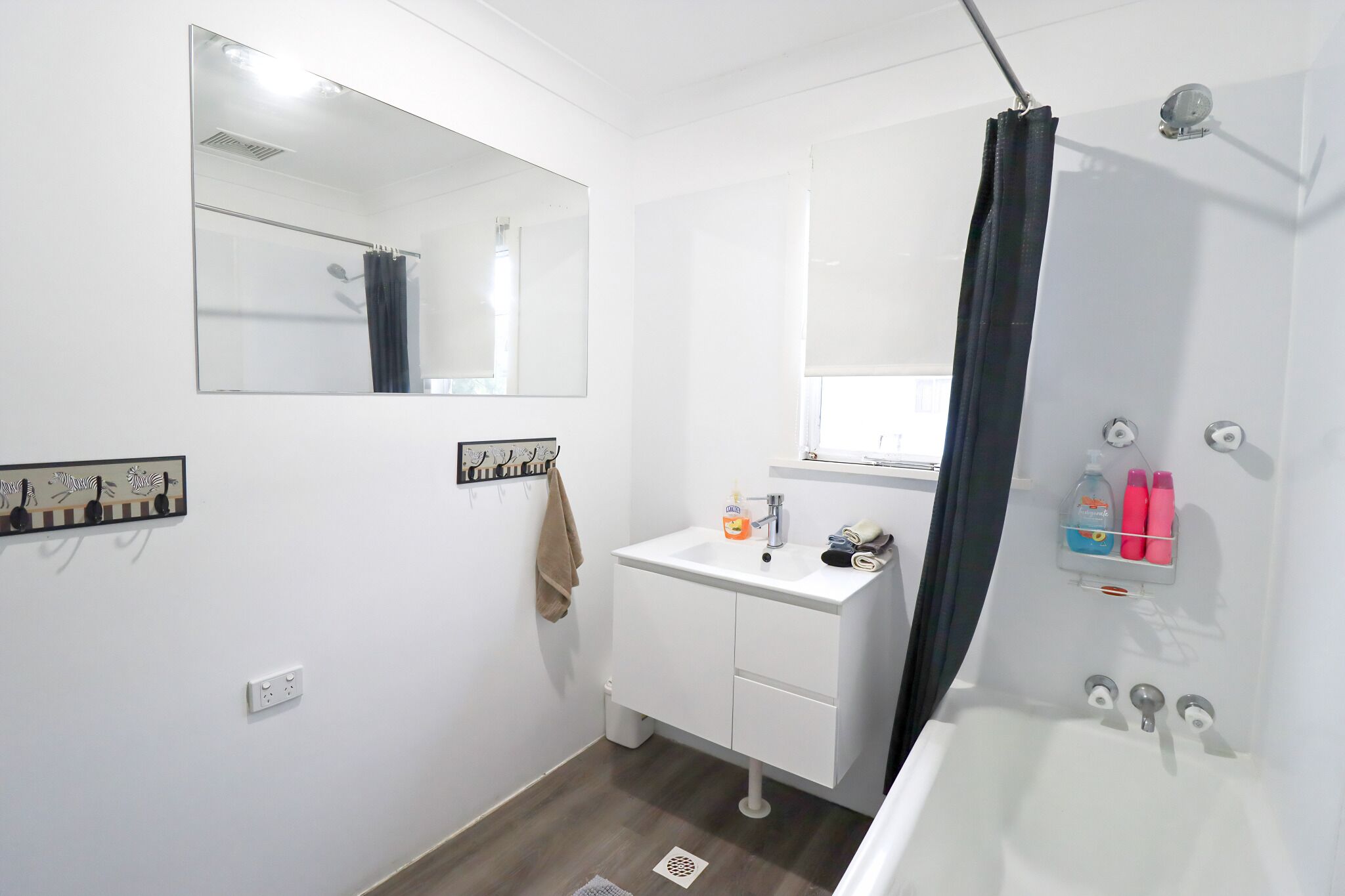 A bathroom with a white sink, mirror, shower, and a towel rack.