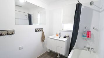 A bathroom with a white sink, mirror, shower, and a towel rack.