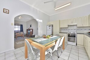 Una cocina moderna con comedor, muebles blancos, horno empotrado y una mesa de vidrio.