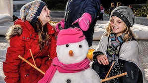 A group of people in winter clothing, including a snowman, in a snowy outdoor setting.