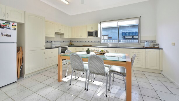 A kitchen with a dining table, chairs, cabinets, a microwave, and a ceiling fan.