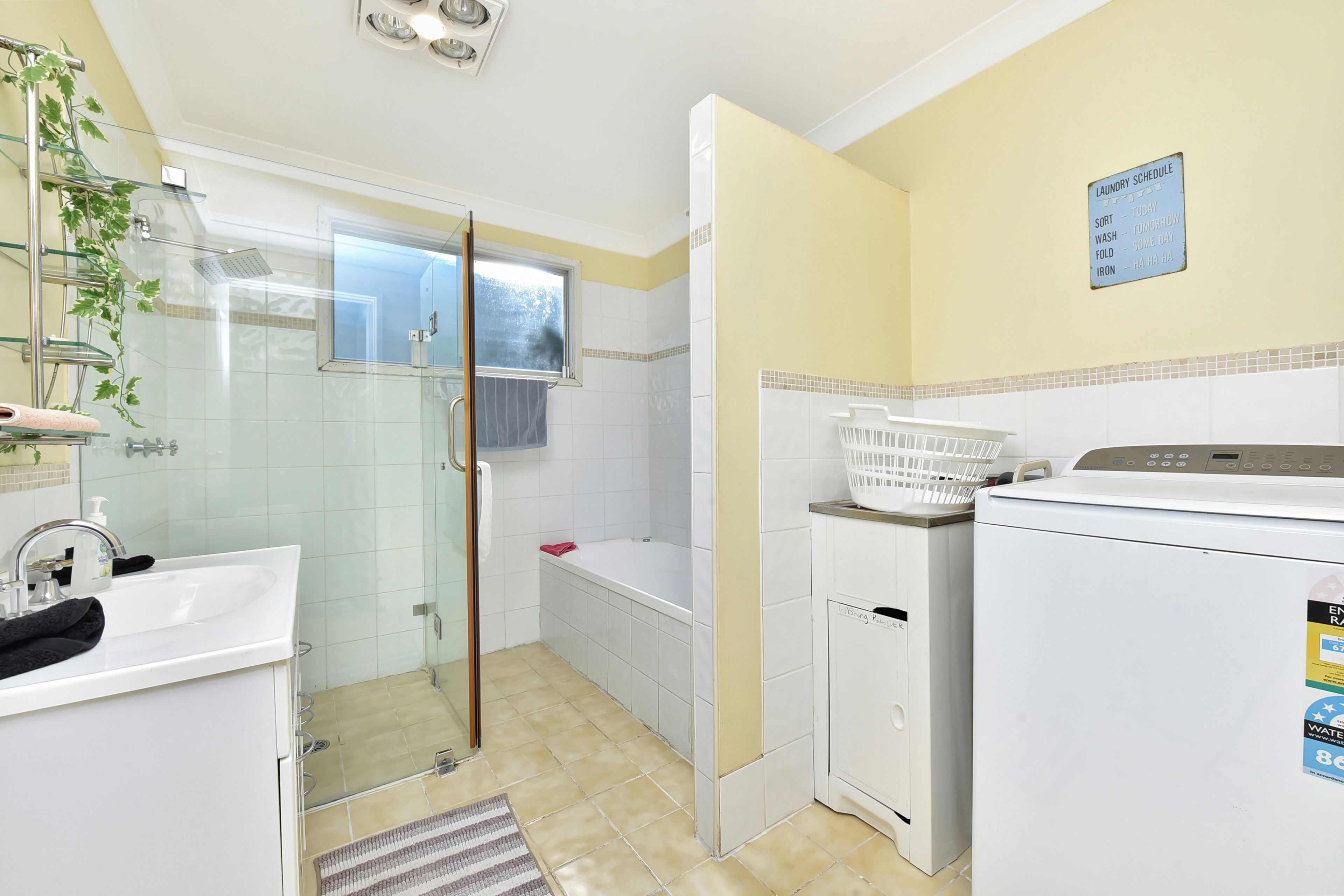 A bathroom with a glass shower enclosure, a white sink, a bathtub, and a laundry area with a washing machine and dryer.