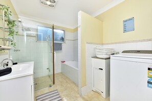 Un baño con cabina de ducha de vidrio, un lavamanos blanco, una bañera y zona de lavandería con lavadora y secadora.