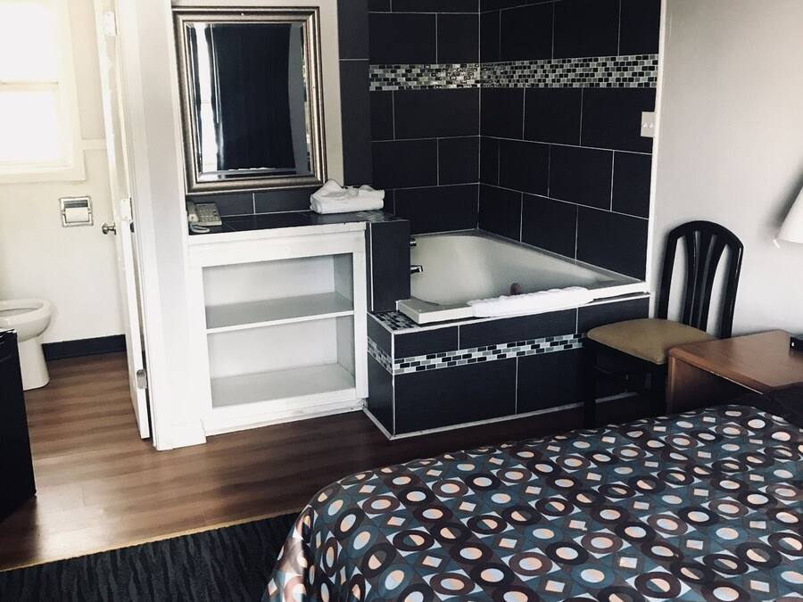 A hotel room with a bed, a small desk, a chair, a bathroom with a bathtub, and a mirror.