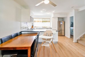 A modern kitchen with a dining table, a high chair, and a refrigerator. - Growder Court 3 - Coolum Beach QLD (Coolum Beach)