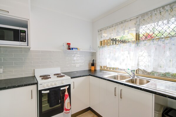 Une cuisine avec des meubles blancs, une cuisinière, un four à micro-ondes et une fenêtre ornée d’un rideau à motifs floraux.