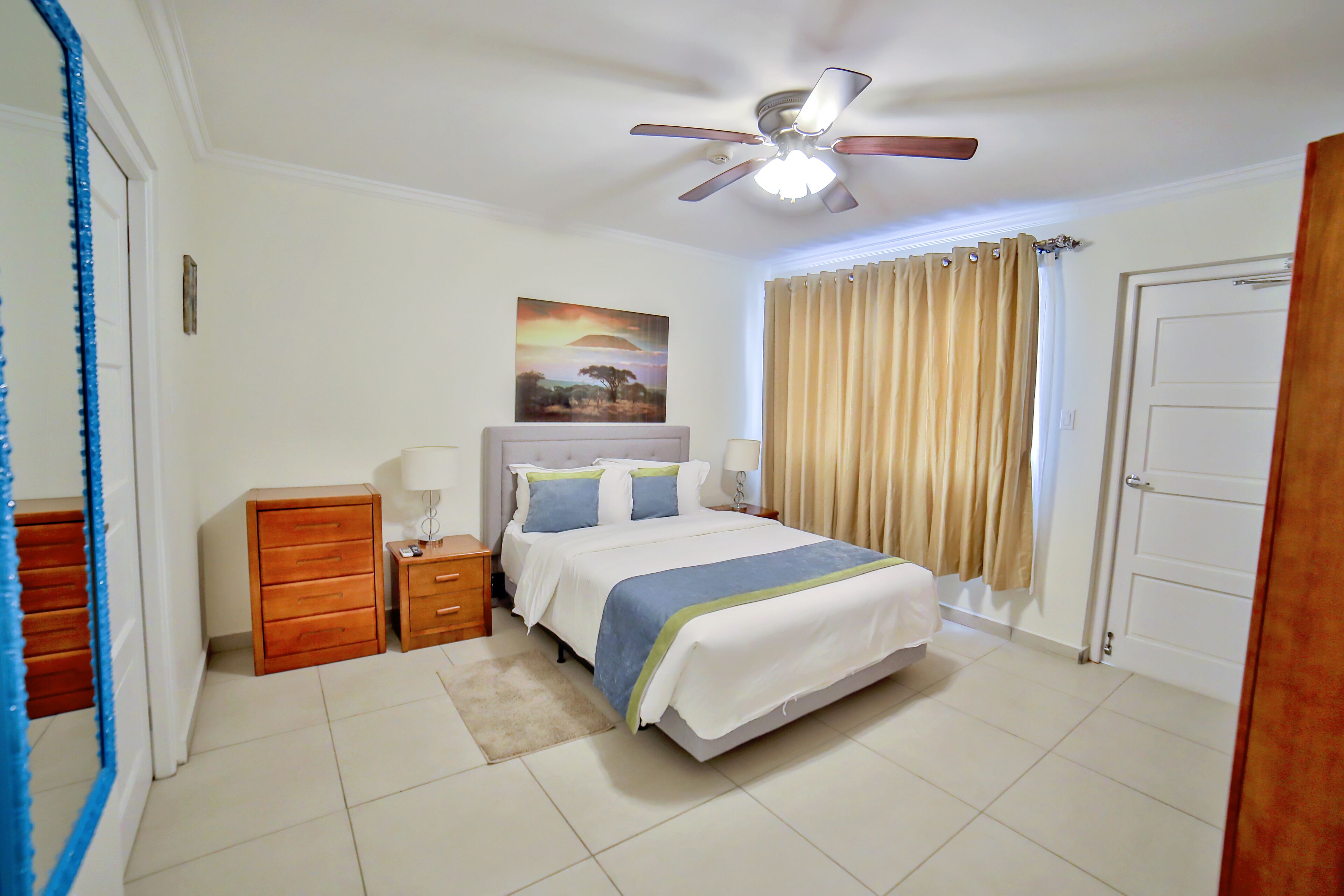 A bedroom with a bed, a nightstand, a dresser, a ceiling fan, and a door.
