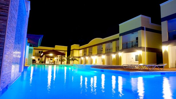 Un área de piscina iluminada de noche con un edificio al fondo.