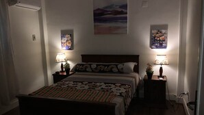 A bedroom with a bed, two bedside tables with lamps, a painting on the wall, and an air conditioning unit. - Heliopolis Apartment (Cairo)