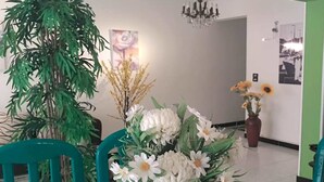 A dining area with a table set for four, surrounded by teal chairs. There is a large potted plant to the left and a vase with white flowers on the table. - Heliopolis Apartment (Cairo)