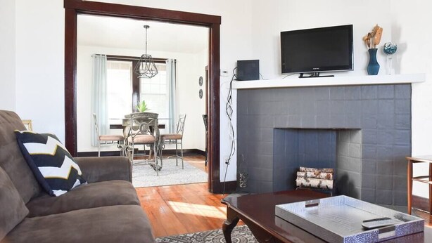 A living room with a sofa, a coffee table, a fireplace, and a TV on a mantel. - Beautiful 3BR Home with Cozy Front & Back Porches! (Munhall)