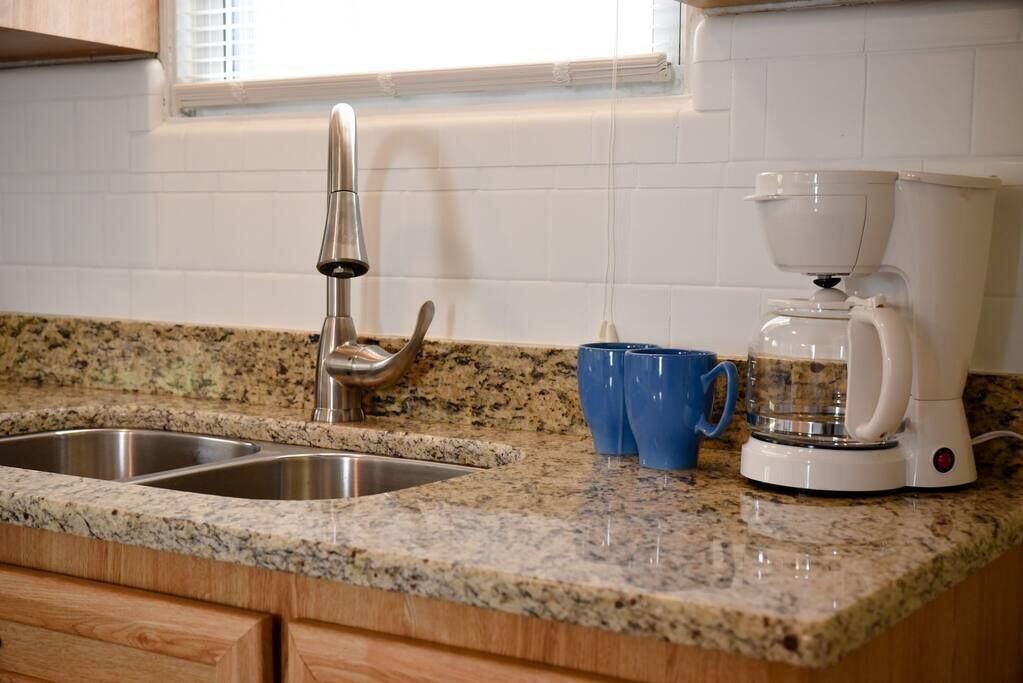 A kitchen with granite countertops, stainless steel sinks, and a coffee maker.