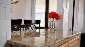 A kitchen with a granite countertop, wooden cabinets, and a vase with orange flowers on the counter. - Beautiful 3BR Home with Cozy Front & Back Porches! (Munhall)