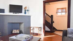 A living room with a fireplace, a television, and a staircase leading to another room. - Beautiful 3BR Home with Cozy Front & Back Porches! (Munhall)