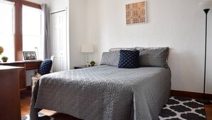 A bedroom with a large bed, a desk, a lamp, and a window with curtains. - Beautiful 3BR Home with Cozy Front & Back Porches! (Munhall)