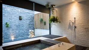 A modern bathroom with a stone wall, a wooden panel, a bathtub, and a shower area. - Shu Shia Motel (Taichung)