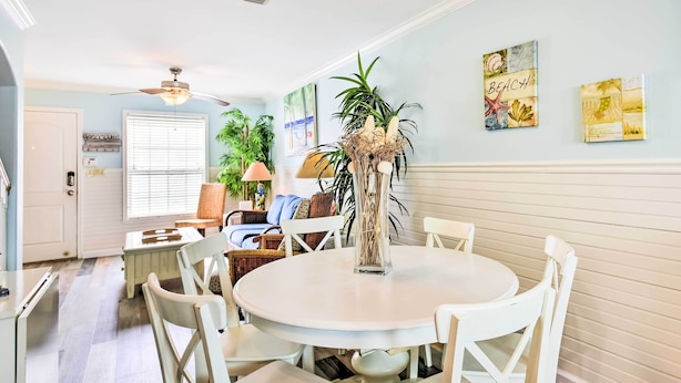 A dining area with a round white table and white chairs, a ceiling fan, and a wall with artwork. - Near Port Aransas Beach: Condo w/ Pool Access (Port Aransas)