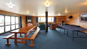 Een kamer met houten wanden, een groot raam, een houten tafel, een bank en een tafeltennistafel.