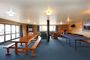 Una habitación con paredes de madera, un ventanal grande, una mesa de madera, un banco y una mesa de ping pong.