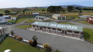 Een motel genaamd 'MOTELS HOLIDAY PARK' met een groot bord, een parkeerplaats en een gebouw met een groen dak.