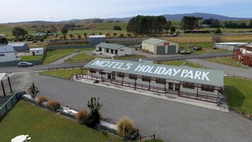 Un motel llamado 'MOTELS HOLIDAY PARK' con un letrero grande, un estacionamiento y un edificio con techo verde.