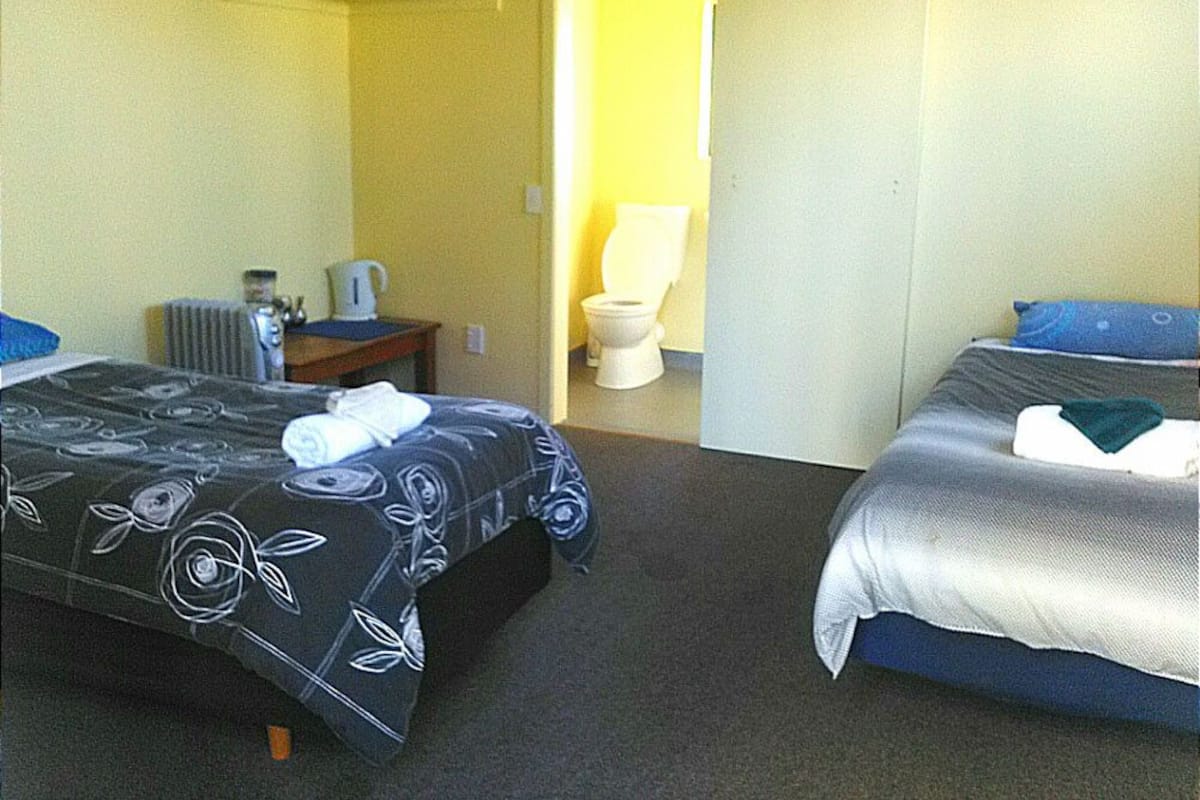 Ein Hotelzimmer mit zwei Betten, einem Heizkörper, einem kleinen Tisch mit Wasserkocher und einer durchgehenden Tür erkennbaren Toilette.