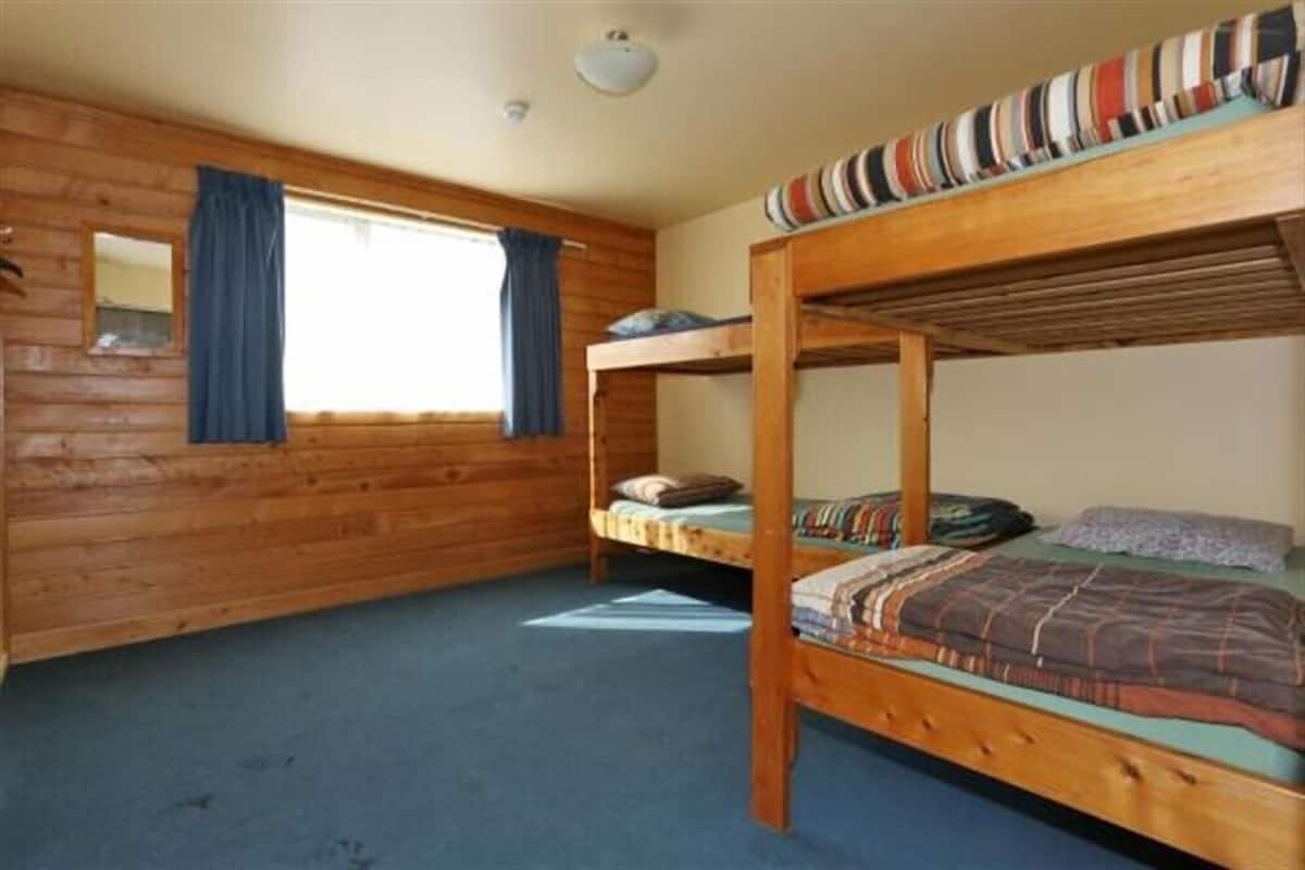 Ein Zimmer mit zwei Etagenbetten, Holzwänden, einem Fenster mit Vorhängen und einer Deckenleuchte.