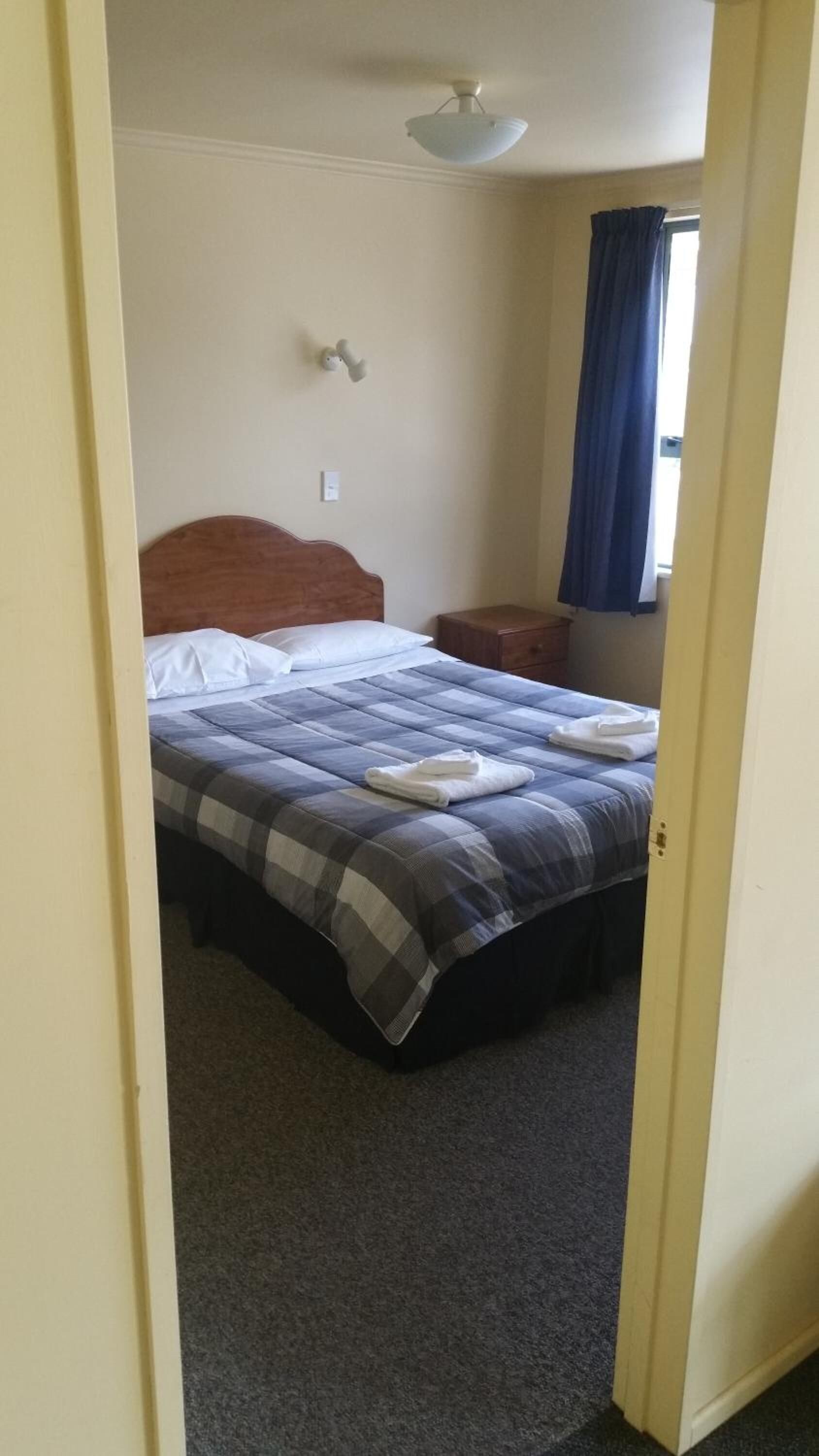 Quarto com cama, mesa de cabeceira, ventoinha no teto e janela com cortinas.