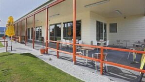 Een overdekt buitengebied met tafels en stoelen, een gele parasol en een grindpad.