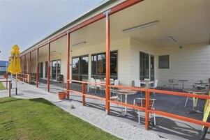 Un espacio al aire libre techado con mesas y sillas, una sombrilla amarilla y un camino de grava.
