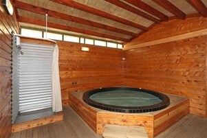 Una cabaña de madera con jacuzzi, zona de ducha y ventana para luz natural.