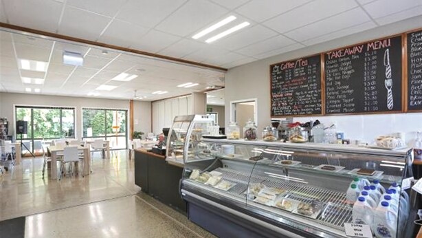 Een cafetaria met een glazen vitrine vol etenswaren, een prikbordmenu en een zithoek met tafels en stoelen.