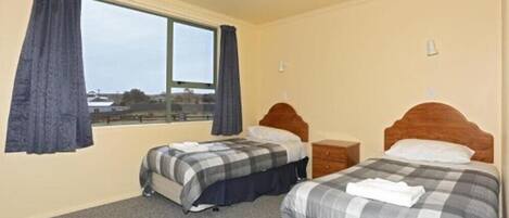 A hotel room with two beds, a window with curtains, a wooden headboard, and a carpeted floor.