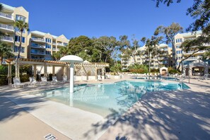 Un espace piscine d’hôtel avec des chaises longues, une pergola et une piscine à l’eau d’un bleu limpide.