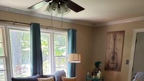 Een woonkamer met een donkergrijze bank, een bijzettafeltje met decoratieve objecten, een lamp en een gitaar schilderij aan de muur.