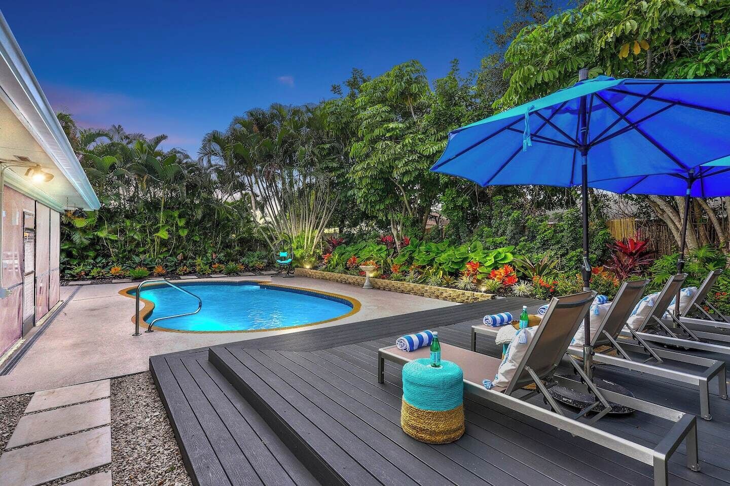Zona de piscina con alberca, sillas de descanso y una sombrilla azul.